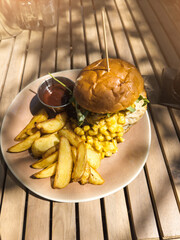 Vertical photo of Tasty food on the table in outdoors street restaurant. Burger with fry potato slices, corn and chicken meat.