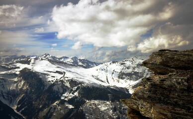 Obraz premium querformat, schneebedeckte berge, massive wolkenbank, blauer himmel, gebirgskette, bad hofgastein, vordergrund granitfelsen, österreich