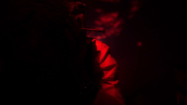 A man in a scary mask of an evil creature close-up. Red flickering light. Twilight. Demon mask on the face of a man with hands near his face. High quality FullHD footage