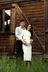 Obraz na płótnie Canvas beautiful pregnant couple on the background of a wooden ecological house in the forest. a man hugs a pregnant woman.