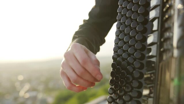 A man plays the accordion at sunset with a view of the city. Close up