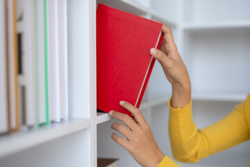 Close-up of woman selecting book from a bookshelf. University student selecting book from library...