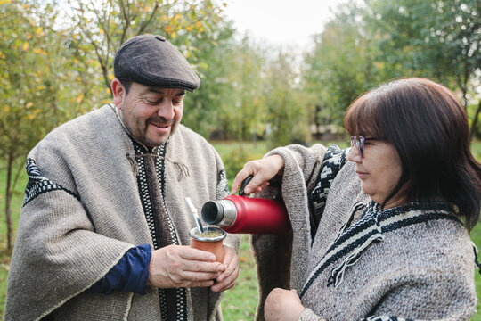 Friends in woolen ponchos sharing hot tea in park