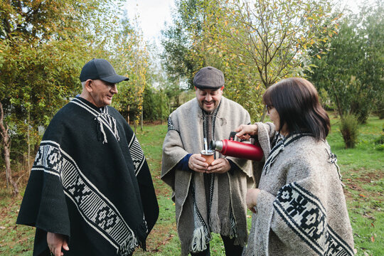 Friends in woolen ponchos sharing hot tea in park