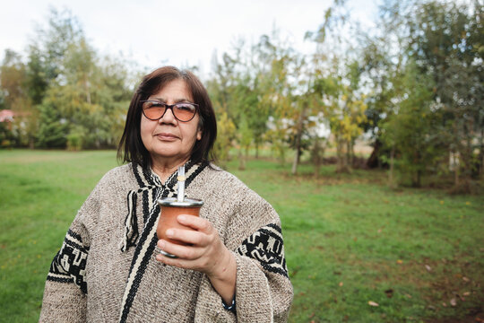 Calm senior woman in traditional clothes drinking mate in park