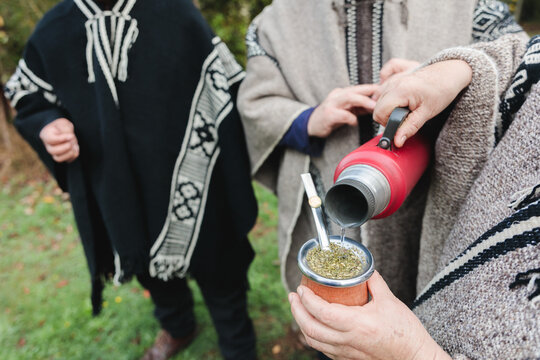 Cropped people in woolen ponchos sharing hot tea in park
