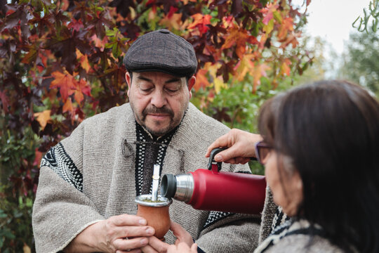 Anonymous female serving hot yerba mate to a serious male while standing in autumn garden in Temuco
