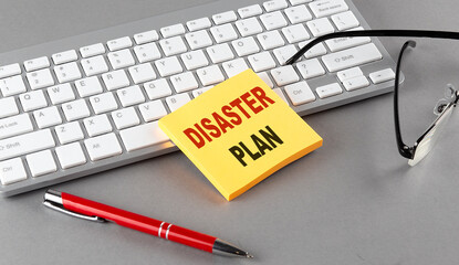 DISASTER PLAN text on a sticky with keyboard, pen glasses on grey background