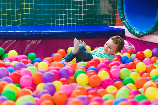 Happy laughing child laughing in an indoor play center. Children playing with colored balls in the playground ball pool. Party