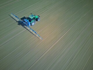 zielony traktor jedzie przez pole i opryskuje. Rozmycia ruchu pokazują jego prędkość