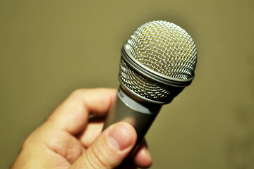 A person's hand holds a mic to amplify the voice, close-up