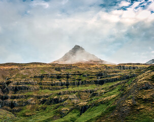 Rugged volcanic pyramid shape and Klifbrekkufossar multi waterfall in Mjoifjordur fjord on summer