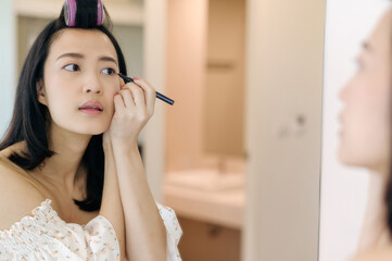 Beautiful young Asian woman applying makeup in front of the mirror. Lifestyle people concept. Advertisement for skin cream, anti-wrinkle cream, baby face