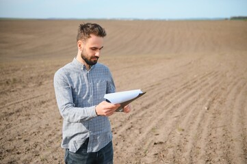 A farmer in boots works in a field sown in spring. An agronomist walks the earth, assessing a...