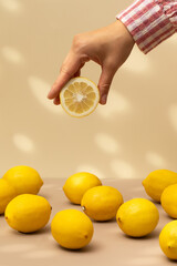 A woman takes half a juicy lemon from the table on a beige background with shadows. Summer, exotic fruits.