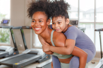 woman with daughter Riding on mom's back after healthy yoga workout in gym, smiling.