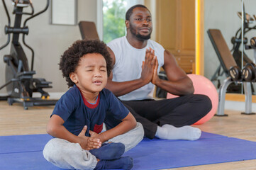 Cute boy in sportswear with her smiling black african american dad meditating on a yoga mat