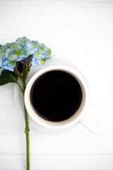 Obraz na płótnie Canvas A cup of coffee and hydrangea flowers on a white wooden background