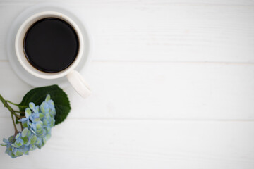 A cup of coffee and hydrangea flowers on a white wooden background