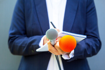 News reporter at media event or press conference, holding microphone, writing notes. Broadcast...