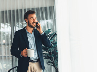 Hardworking businessman stand confidently in modern office making persuasive sales call to client. Office worker talking on the phone coordinate and manage business work with colleagues. Entity