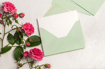 Feminine invitation or greeting card mockup with empty and green envelope and pink roses bouquet on light background.