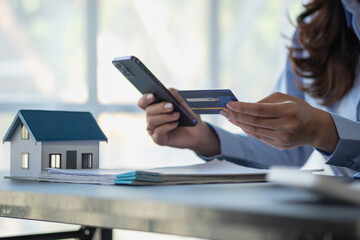 Asian woman with long hair in the blue shirt is using a credit card for buying a new house and looking at home-buying documents The idea of purchasing a home with a credit card.