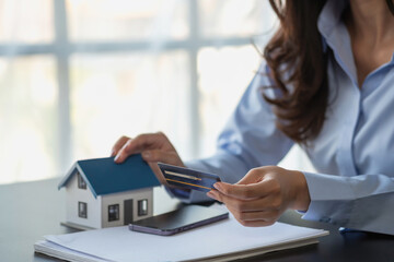 Asian woman with long hair in the blue shirt is using a credit card for buying a new house and looking at home-buying documents The idea of purchasing a home with a credit card.