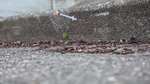 Plastic hypodermic needle dropping into a dirty city gutter; drug epidemic theme; 1000fps slow motion video clip