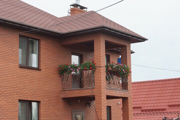brown attic of a private house with an open iron balcony under a tiled roof on the street against the sky