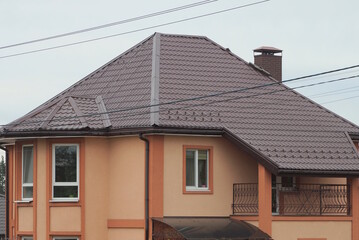 brown attic of a private house with an open iron balcony under a tiled roof on the street against the sky