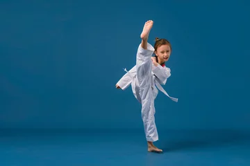 Foto op Plexiglas Banner: Asian-Australian girl poses in martial arts Practice taekwondo, karate, judo against a blue background in the studio. Asian kids karate or Taekwondo martial arts. Sport kid training action. © VR Studio