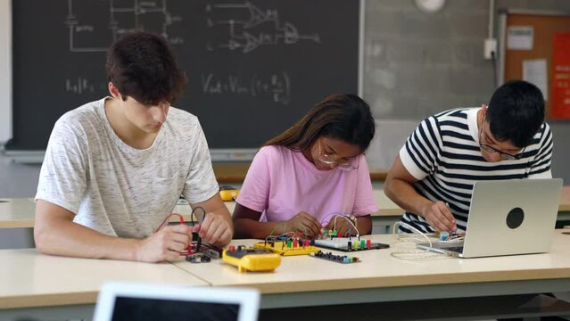 Diverse high school students group working on electronic project in science robotics lesson using laptop computer education software app. Classmates learning to build electronic circuits at classroom.