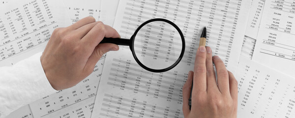 Woman holding a magnifying glass pointing at numbers on financial documents. ?oncept of finance, search and accounting.