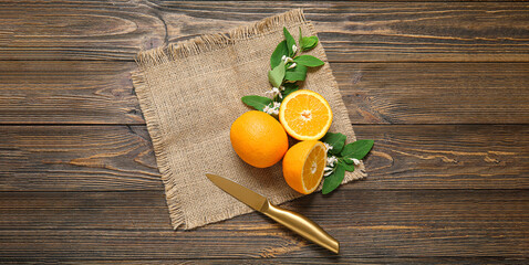 Fresh oranges with blooming branches, knife and sack cloth on wooden table