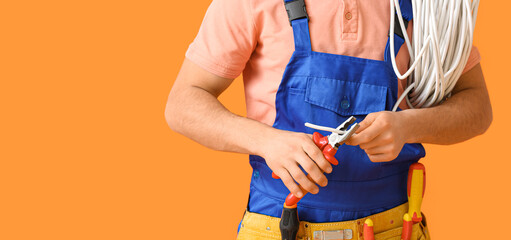 Young electrician with pliers and cable on orange background, closeup