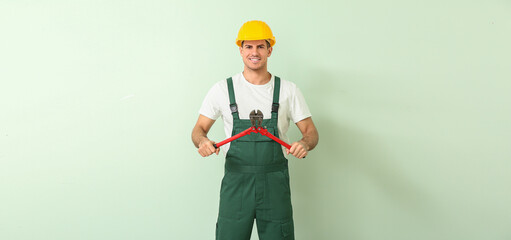 Handsome male worker with bolt cutter on light green background