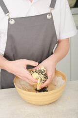 male chef holding and kneading cookie dough with chocolate chips. vertical shot of teenager boy cooking traditional american cookies.