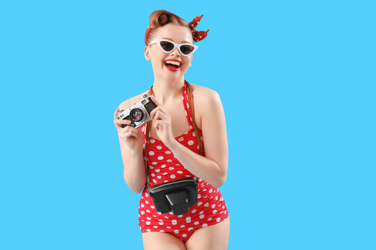 Young pin-up woman in swimsuit with photo camera on blue background