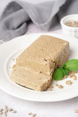 Plate with tasty halva and sunflower seeds on white background