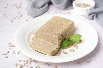 Plate with tasty halva and sunflower seeds on white background