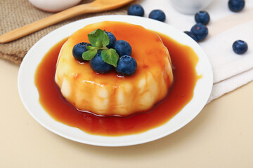 Plate with delicious pudding, blueberries and mint covered by caramel syrup on beige background