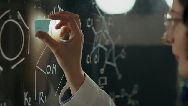Microbiology, Middle-aged male doctor Concentratedly glues a note on a glass board in a scientific institute. Microbiologist Creates cures for diseases Creates a learning strategy, write formulas
