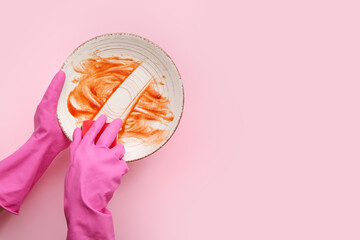 Female hands in rubber gloves washing dirty plate with sponge on pink background