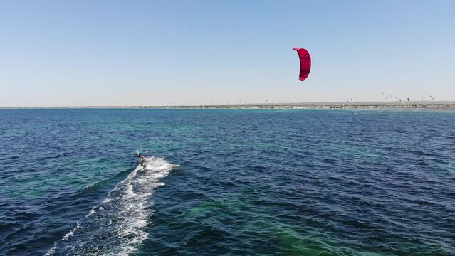 Aerial view of a kitesurfer off the coast. Drone footage of woman kitesurfer cutting waves at high speed while sailing, water sport