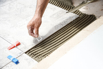 The hands of the tiler are laying the ceramic tile on the floor.