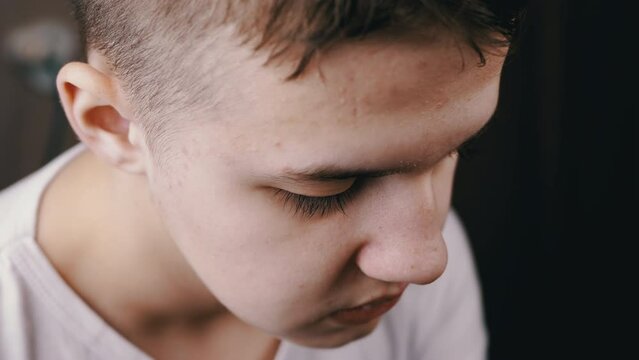Close up, Sad, Upset, Offended Child Looking Down on Isolated Blurred Background. Portrait of the face of a lonely, guilty teenager with a downcast look, eyes, sitting in a room. Protest, punishment.