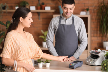 Young woman paying with credit card via banking terminal in flower shop