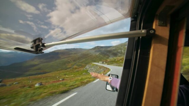 Through the window shot of female driver reach hand out of camper van while driving. Concept of wanderlust road trip and freedom on summer holiday. Scandinavian vacation