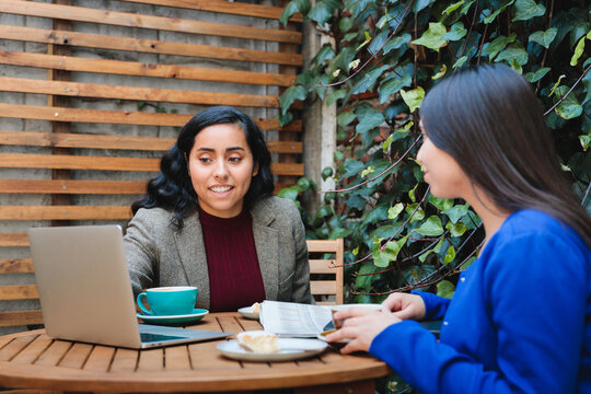 Financial Security Conversation: Young Latina Woman Selling Life Insurance to Another Woman at a Cozy Cafe